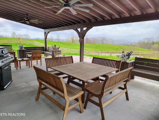 view of patio featuring a rural view, outdoor dining space, ceiling fan, a mountain view, and fence