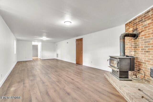 unfurnished living room with wood finished floors, a wood stove, and baseboards