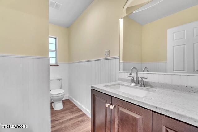 bathroom with vanity, toilet, wainscoting, visible vents, and wood finished floors