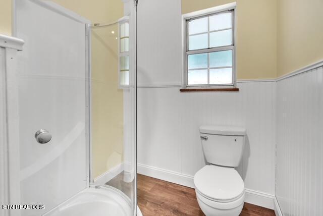 bathroom with a shower, wood finished floors, wainscoting, and toilet
