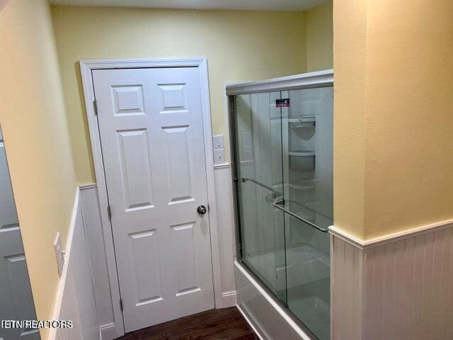 full bath featuring shower / bath combination with glass door, a wainscoted wall, and wood finished floors