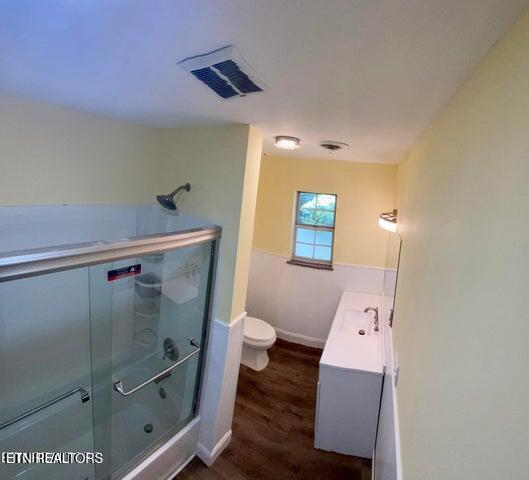 bathroom with visible vents, toilet, vanity, wood finished floors, and a shower with shower door