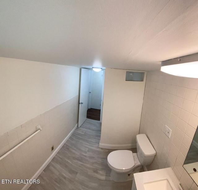 bathroom with toilet, wood finished floors, baseboards, and tile walls
