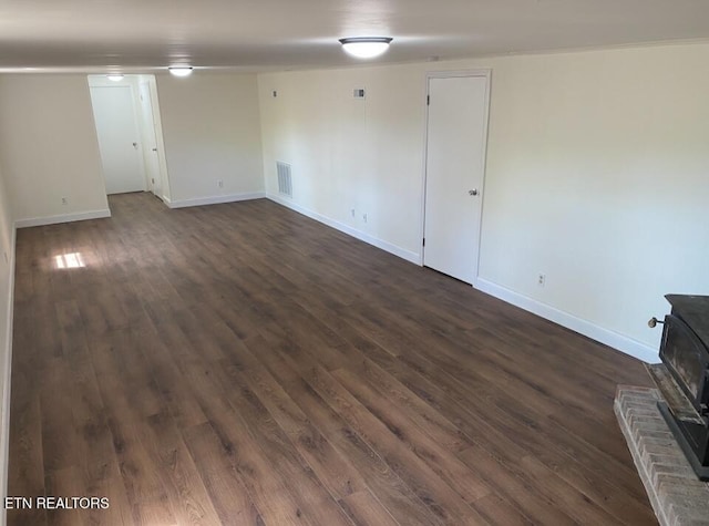 basement featuring a wood stove, dark wood-type flooring, visible vents, and baseboards