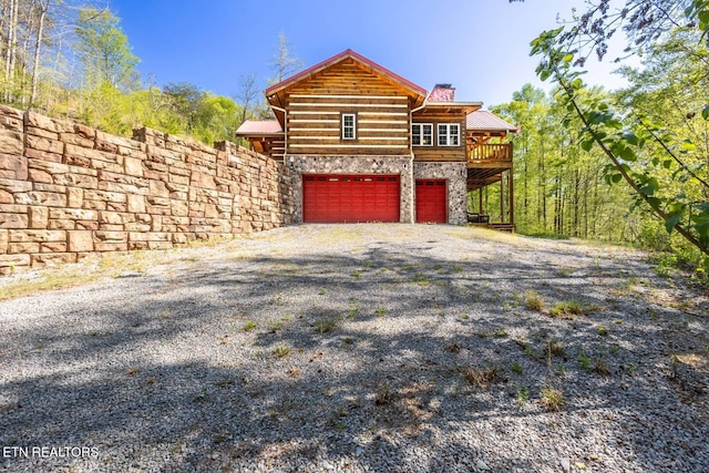 view of front of property featuring a chimney, an attached garage, a wooden deck, driveway, and stone siding