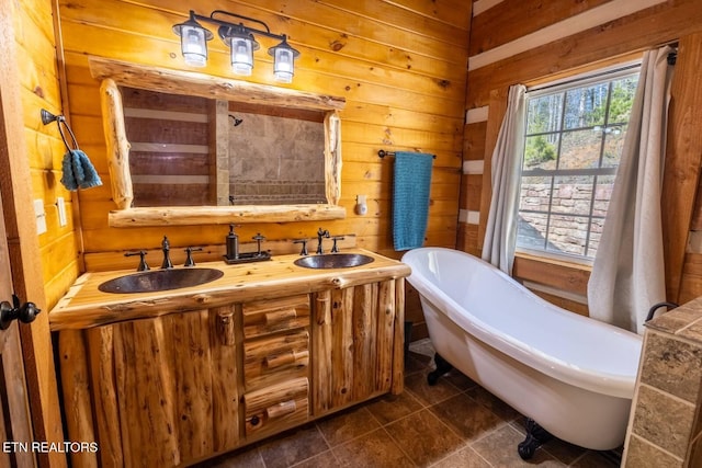 full bath featuring wooden walls, a freestanding tub, tile patterned floors, and a sink