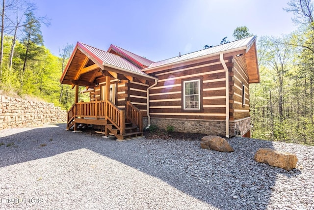 view of side of property with log exterior, a standing seam roof, covered porch, and metal roof