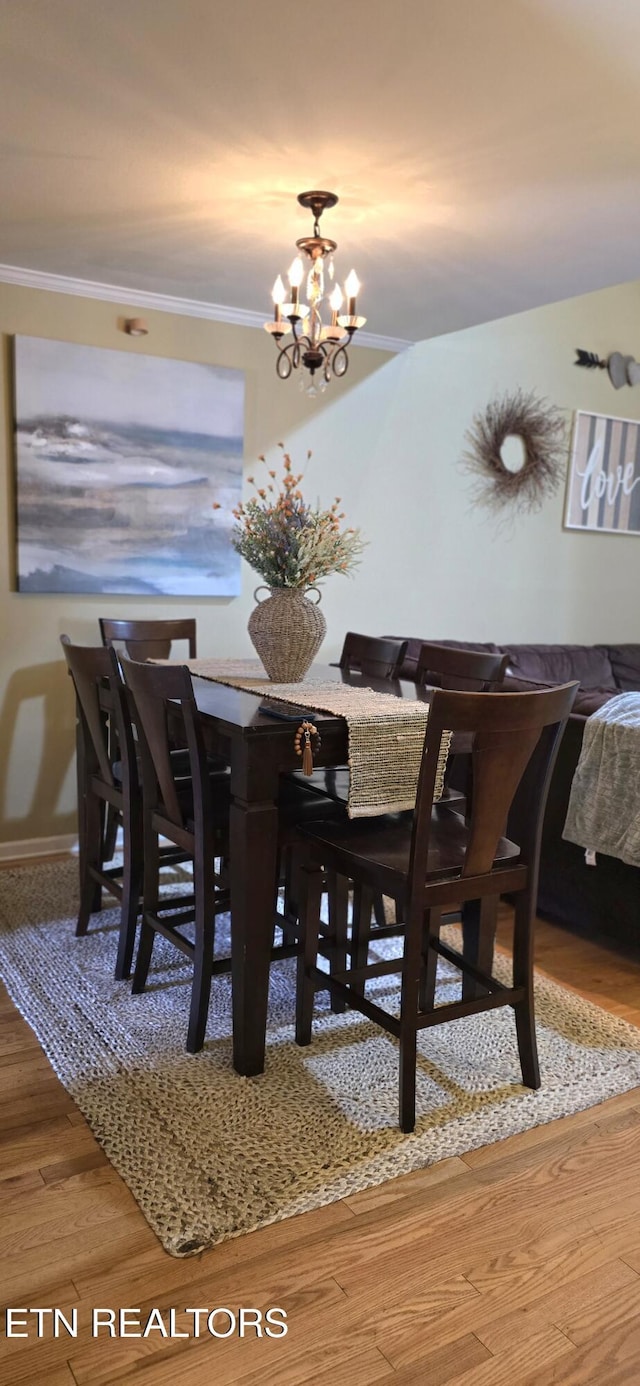 dining space featuring crown molding, wood finished floors, a notable chandelier, and baseboards