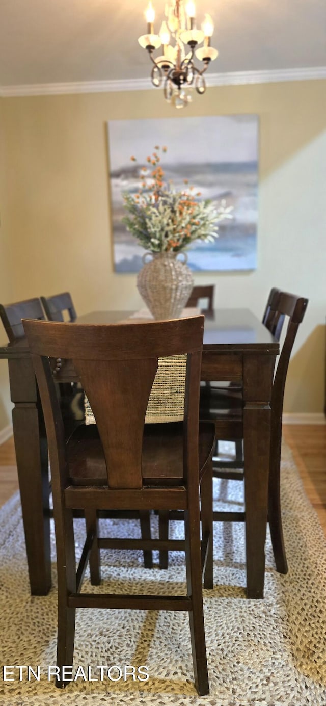 dining space with wood finished floors, crown molding, baseboards, and a notable chandelier