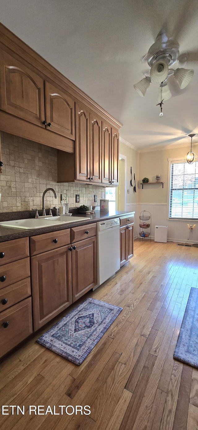 kitchen featuring white dishwasher, backsplash, dark countertops, light wood finished floors, and a sink