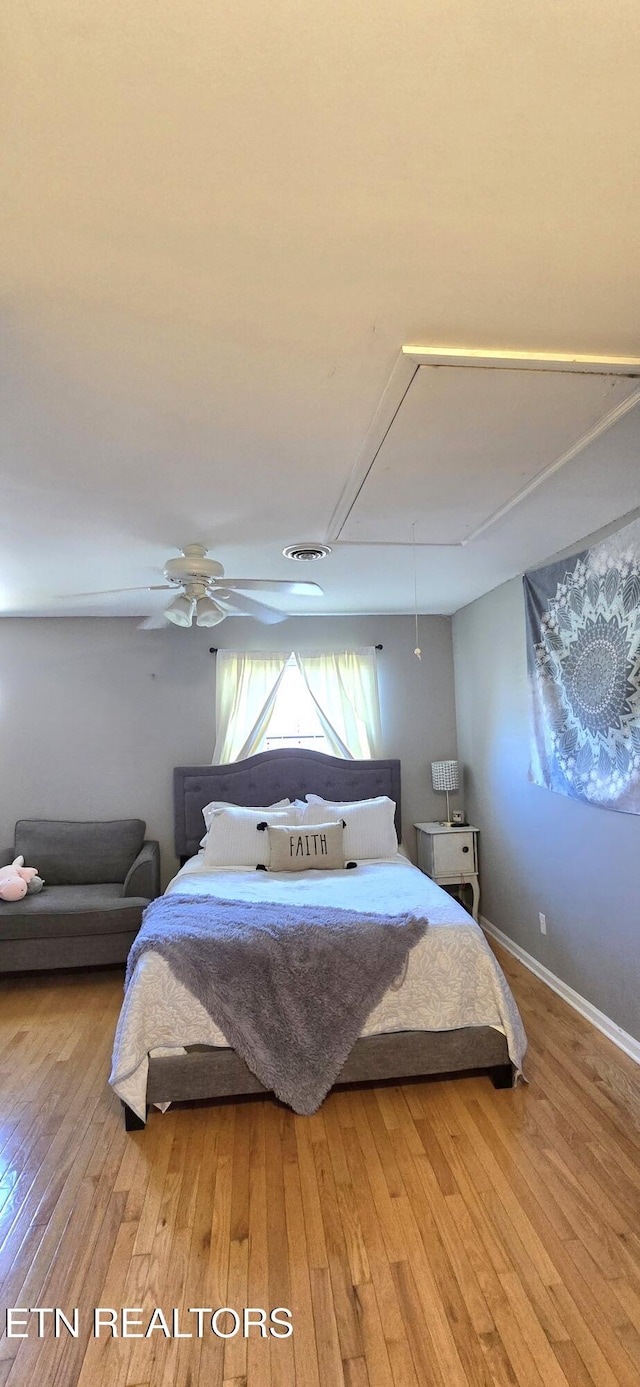 bedroom featuring light wood finished floors, visible vents, attic access, and ceiling fan