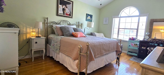 bedroom with baseboards, lofted ceiling, and hardwood / wood-style flooring