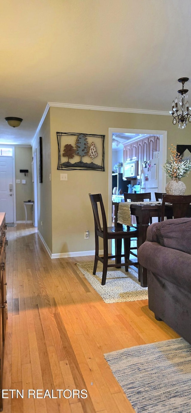 interior space featuring a chandelier, light wood-style flooring, baseboards, and crown molding