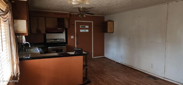 kitchen with tile counters, under cabinet range hood, stainless steel electric stove, a sink, and a ceiling fan