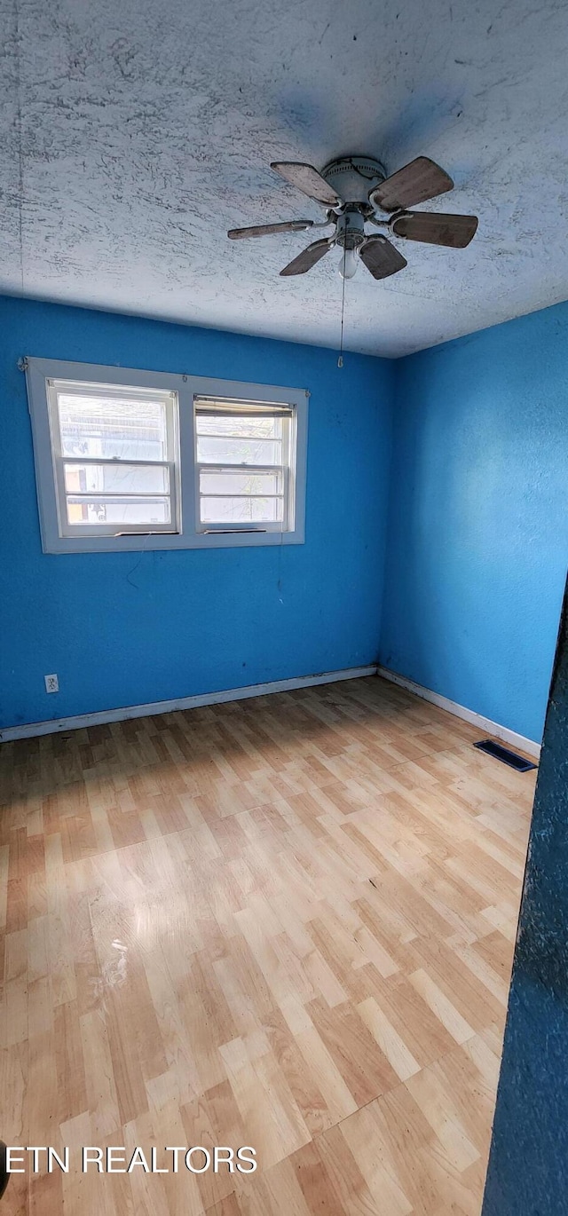 empty room featuring visible vents, a ceiling fan, wood finished floors, and a textured ceiling
