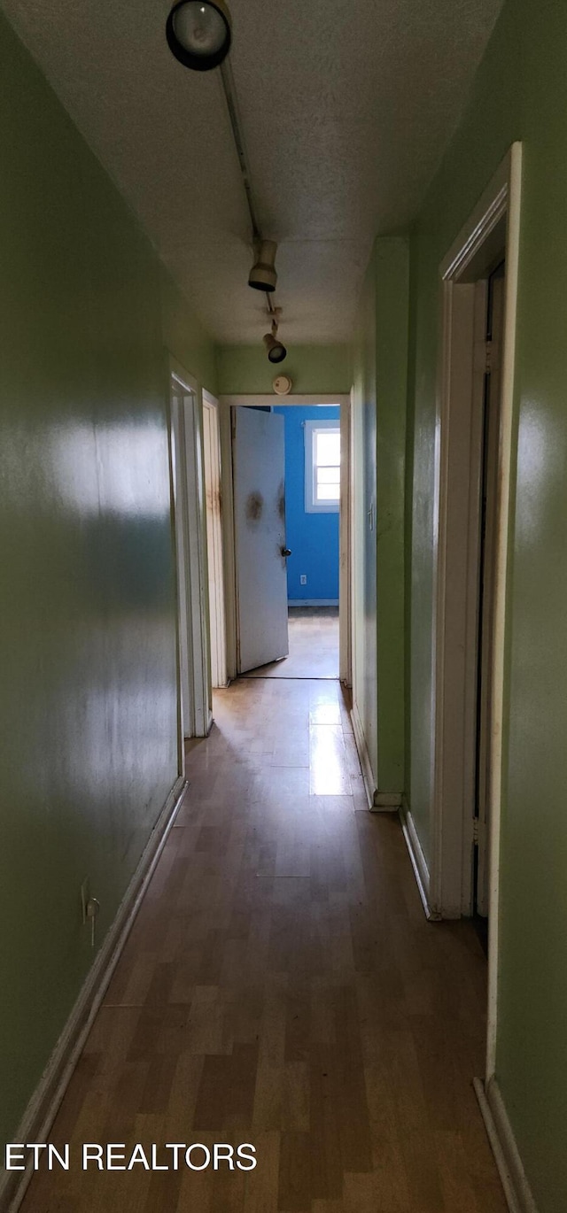 hallway featuring baseboards, wood finished floors, and a textured ceiling