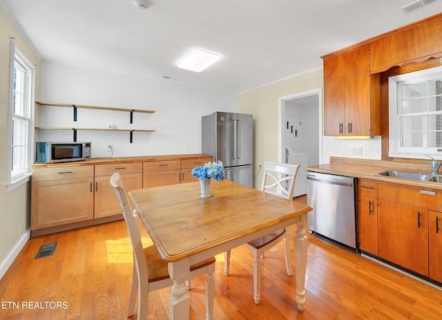 kitchen with a sink, open shelves, tasteful backsplash, light wood-type flooring, and stainless steel appliances