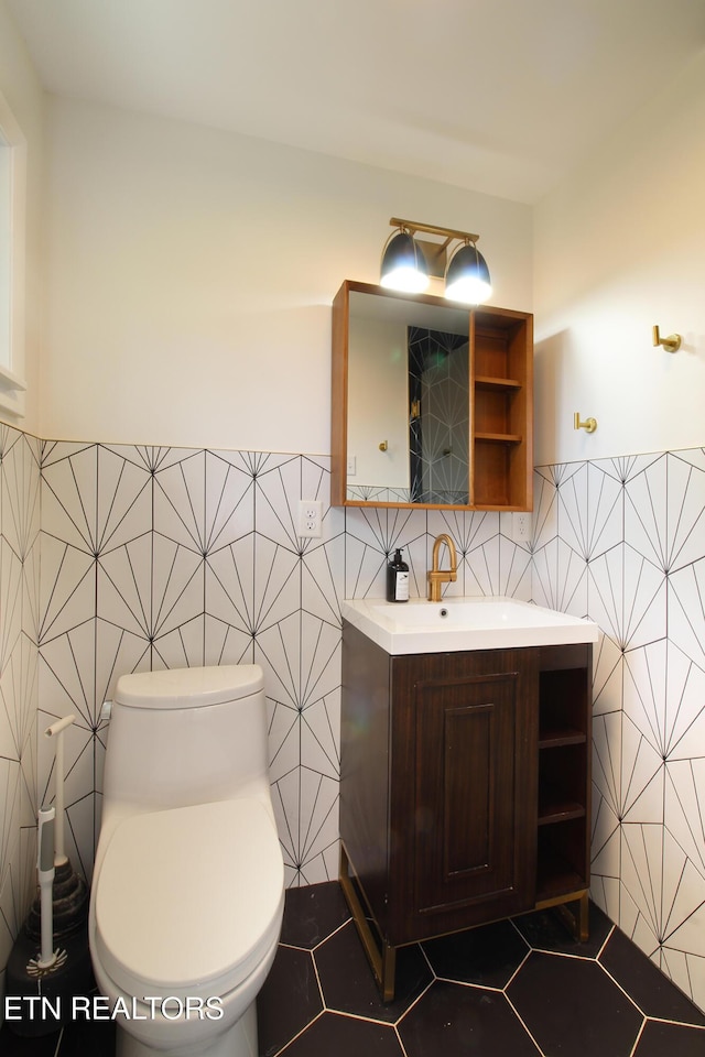 bathroom with tile walls, toilet, vanity, tile patterned flooring, and wainscoting