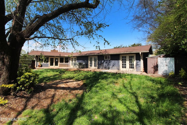 back of property featuring french doors, fence, a storage unit, a lawn, and an outdoor structure