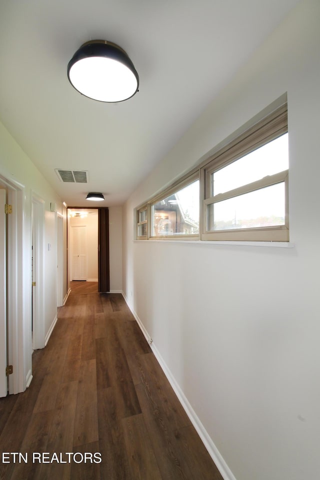 hall featuring baseboards, visible vents, and dark wood-style flooring