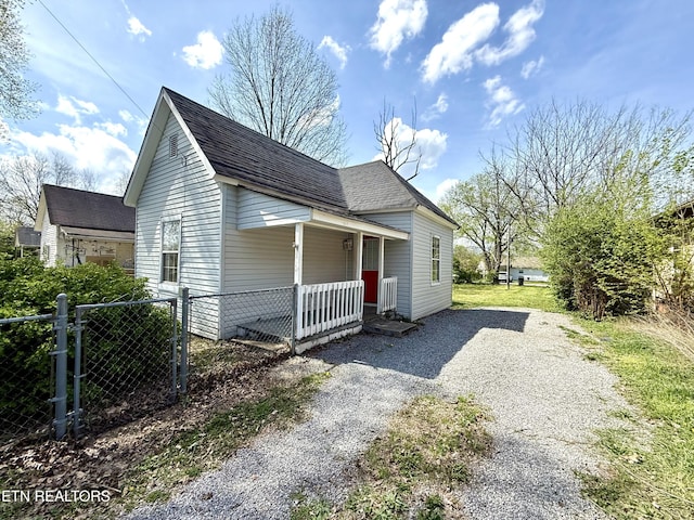 view of side of home featuring a porch, a shingled roof, gravel driveway, and fence