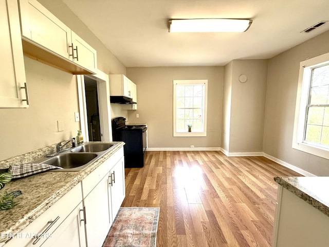 kitchen with baseboards, light wood-type flooring, under cabinet range hood, black range with electric cooktop, and a sink