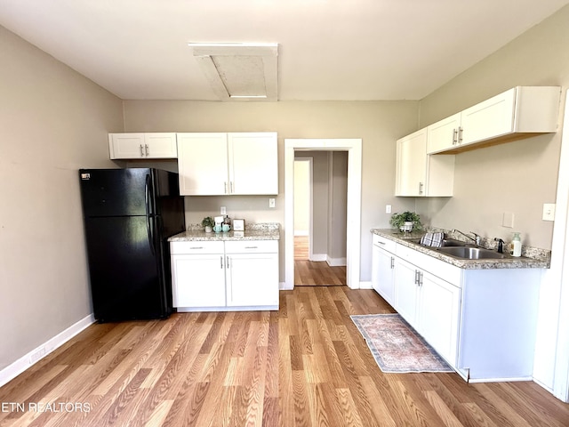 kitchen featuring white cabinets, baseboards, a sink, freestanding refrigerator, and light wood-style floors