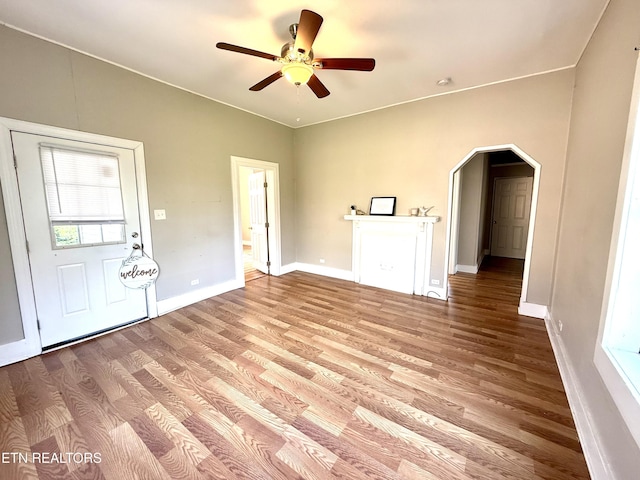 interior space featuring arched walkways, baseboards, a ceiling fan, and wood finished floors