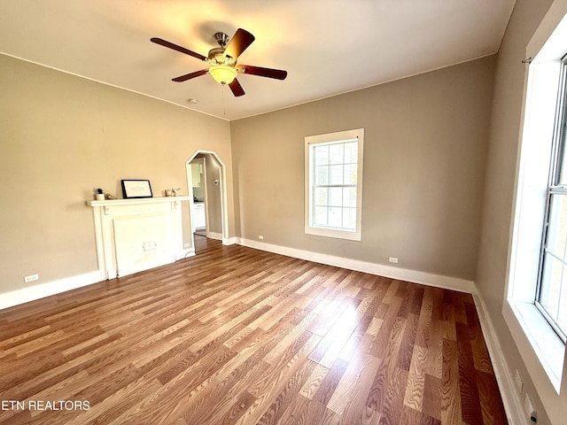 unfurnished room featuring ceiling fan, arched walkways, wood finished floors, and baseboards