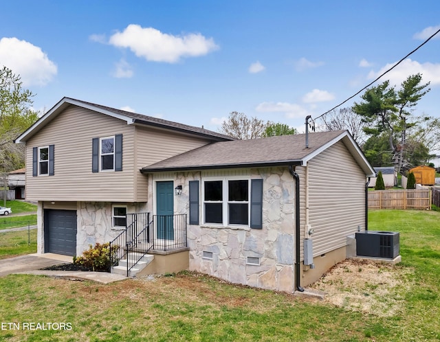 tri-level home with a front yard, stone siding, central air condition unit, an attached garage, and fence