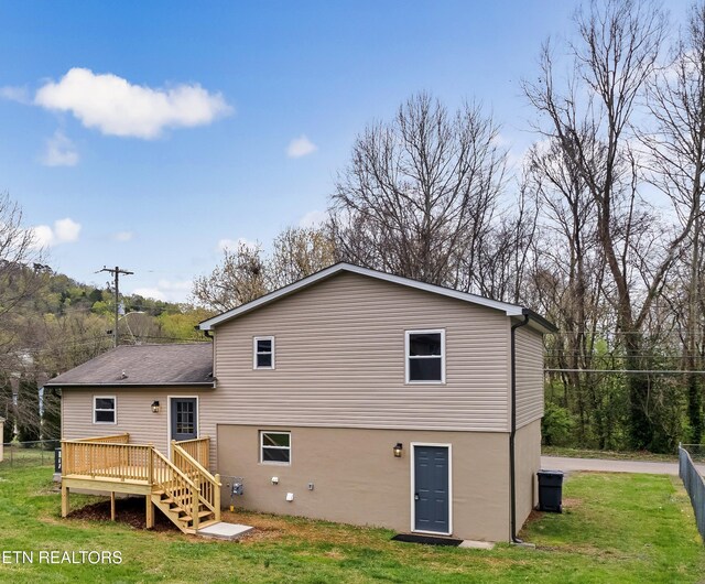rear view of property featuring fence, a deck, and a lawn