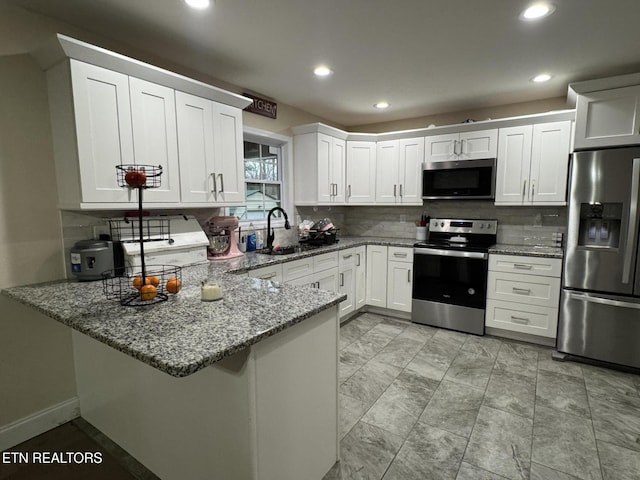 kitchen with light stone counters, a sink, a peninsula, stainless steel appliances, and white cabinets