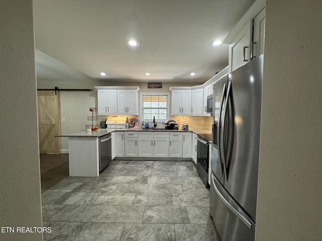 kitchen featuring stainless steel appliances, backsplash, a barn door, white cabinets, and a peninsula