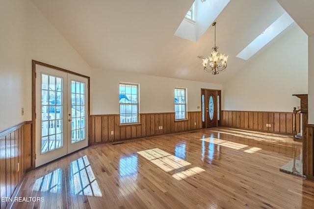 interior space with a wainscoted wall, a notable chandelier, a skylight, and french doors