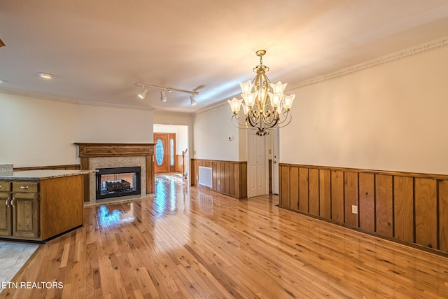 unfurnished living room featuring wainscoting, light wood-type flooring, visible vents, ornamental molding, and an inviting chandelier
