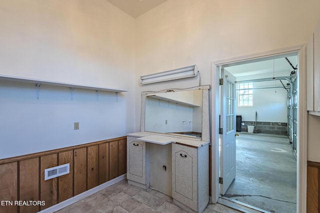 kitchen with a wainscoted wall, light countertops, visible vents, and wood walls