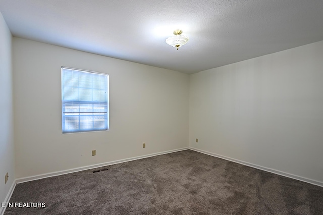 spare room with baseboards, visible vents, and dark colored carpet