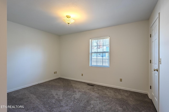 spare room featuring baseboards, visible vents, and dark carpet