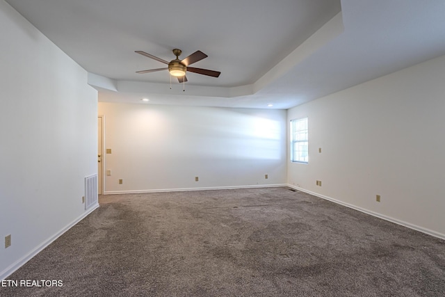 empty room with a ceiling fan, a tray ceiling, baseboards, and visible vents