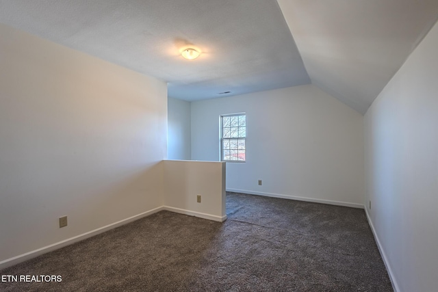 interior space with baseboards, lofted ceiling, and dark carpet