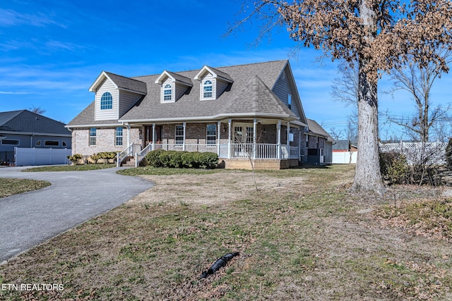 view of front facade featuring a front yard, covered porch, fence, and brick siding