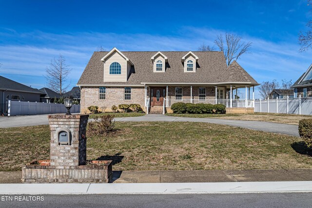 cape cod home featuring fence, a front yard, brick siding, a porch, and a shingled roof