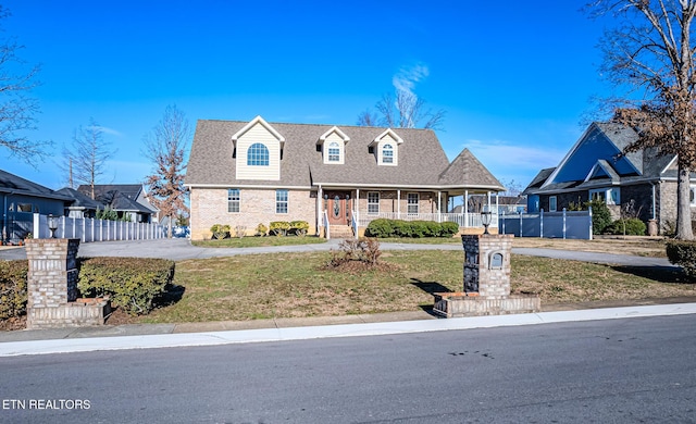 view of front of property with covered porch, brick siding, a front yard, and fence