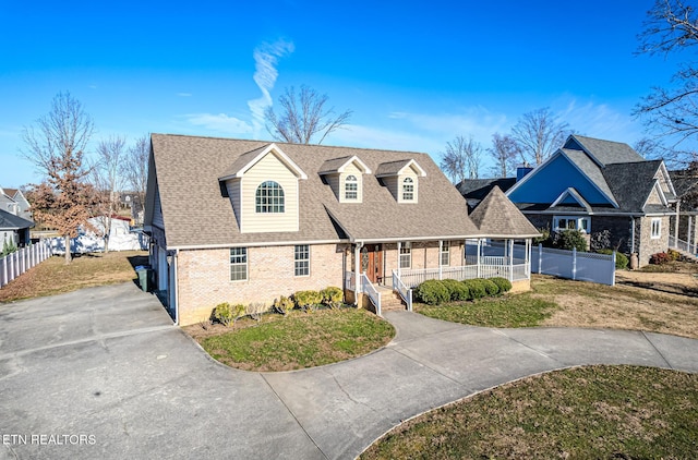 view of front of home featuring driveway, fence, brick siding, a shingled roof, and a porch