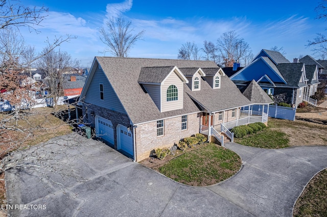 view of front facade with roof with shingles, driveway, a front yard, brick siding, and a porch