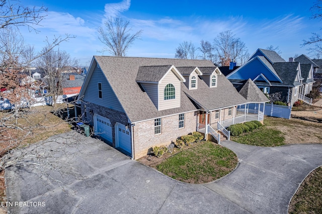 view of front of property with concrete driveway, a front yard, covered porch, brick siding, and a shingled roof