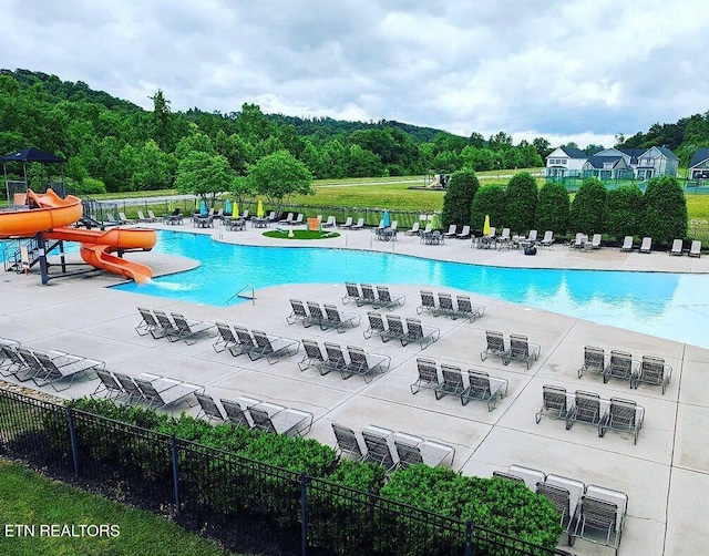 view of swimming pool featuring a water slide, fence, and a patio