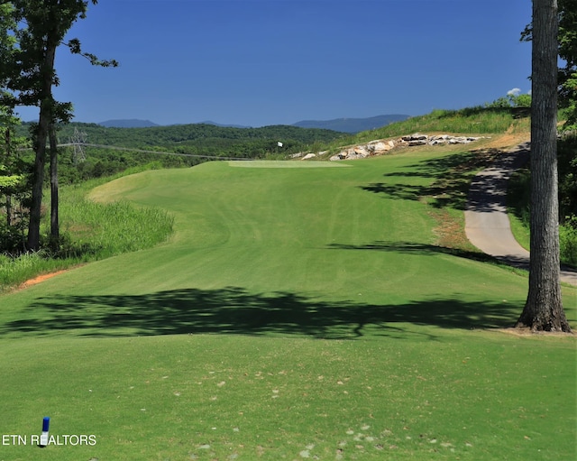 view of property's community featuring a lawn, golf course view, and a mountain view