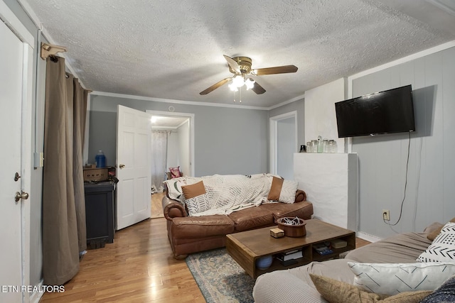 living room with a textured ceiling, ceiling fan, light wood-style floors, and crown molding