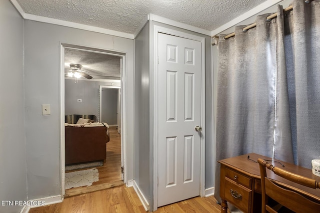 hall with light wood-style flooring, baseboards, and a textured ceiling